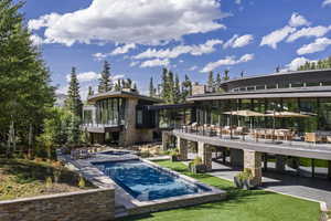 Back of house with a patio area, an outdoor pool, stone siding, and a balcony