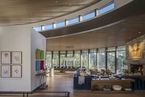 Living area featuring a high wooden ceiling, healthy amount of natural light, wood finished floors, expansive windows, and a stone fireplace