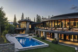 Back of house at dusk with an in-ground hot tub, a patio, an outdoor pool, and a balcony