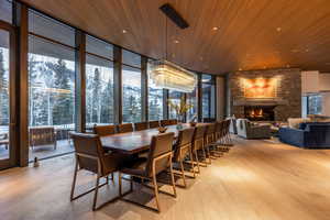Dining room with floor to ceiling windows, light wood finished floors, wooden ceiling, a stone fireplace, and recessed lighting