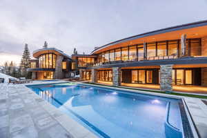 Back of property with a balcony, stone siding, a patio, and an outdoor pool