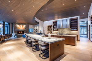 Kitchen featuring open shelves, a breakfast bar, wooden ceiling, open floor plan, and a stone fireplace