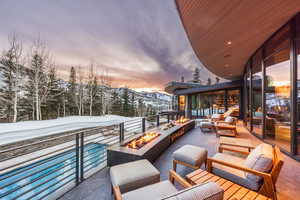 Snow covered back of property with a mountain view and an outdoor living space with a fire pit