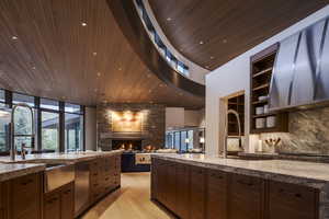 Kitchen with range hood, dark wood finish cabinetry, a fireplace, dark stone counters, and recessed lighting