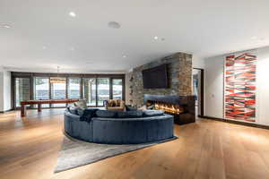 Living room with light wood-style floors, a stone fireplace, billiards table, and recessed lighting