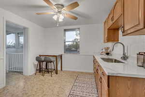 Kitchen featuring light stone countertops, tasteful backsplash, ceiling fan, and light wood finish cabinets