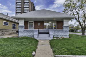 View of front of home with covered porch, a front yard, and stone siding
