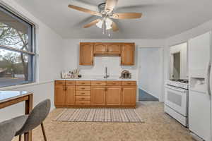 Kitchen featuring light countertops, white appliances, ceiling fan, and wood finish cabinetry