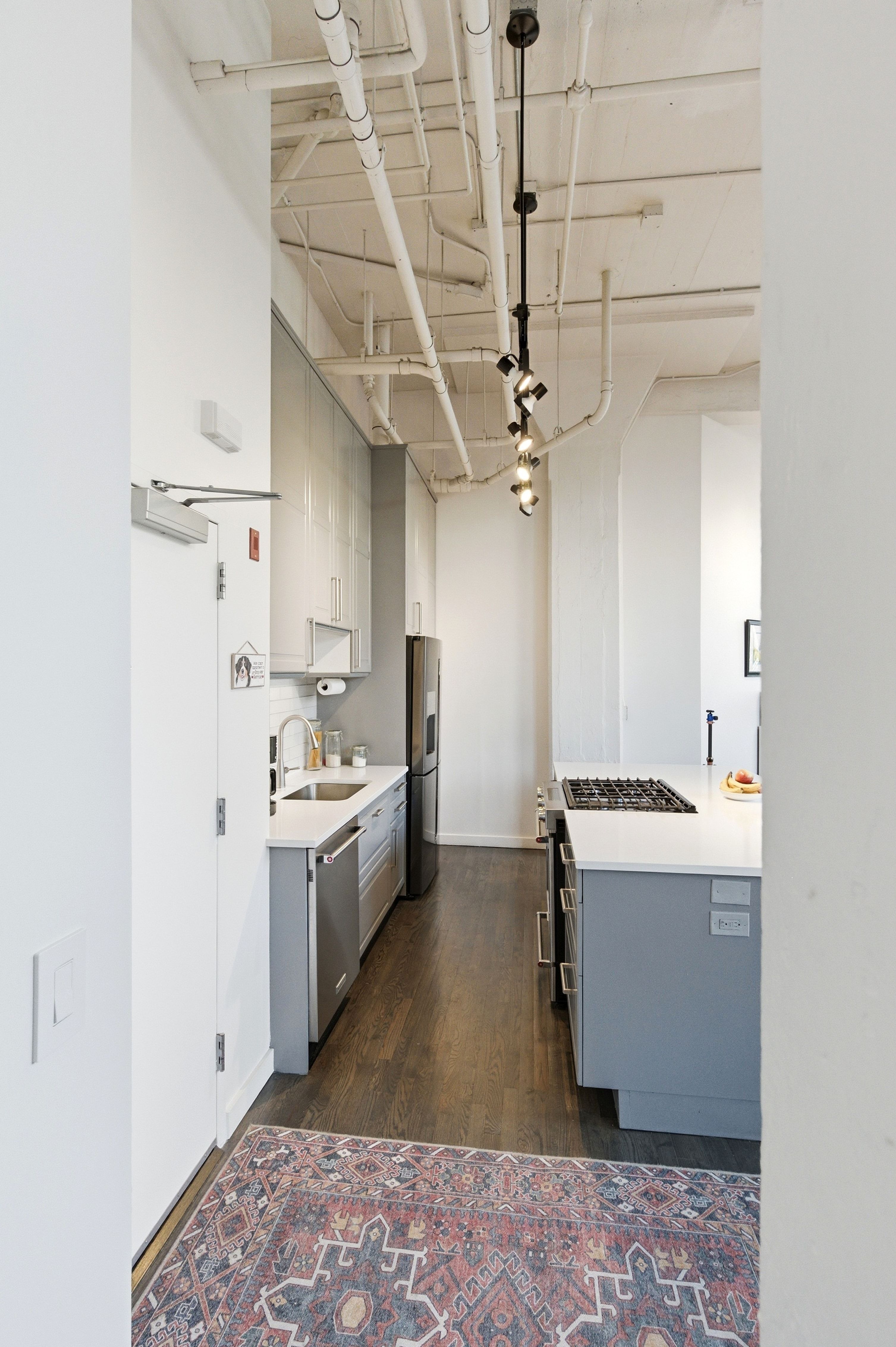 Dual tone kitchen featuring dark wood finished floors, two tone color scheme, stainless steel appliances, pendant lighting, and light stone countertops