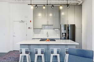 Kitchen featuring gray cabinetry, a kitchen bar, a center island, tasteful backsplash, and stainless steel gas cooktop