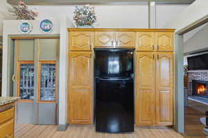 Kitchen with freestanding refrigerator, a brick fireplace, and light wood-type flooring