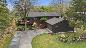 View of front of house featuring roof with shingles, concrete driveway, a deck, a garage, and a front yard