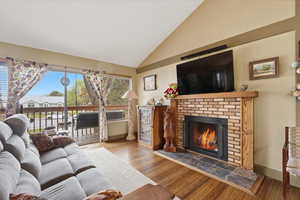 Living room with vaulted ceiling, wood finished floors, and a brick fireplace