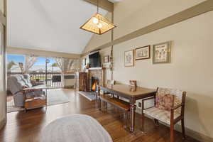Dining space featuring a brick fireplace, dark wood-style flooring, and lofted ceiling