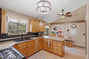Kitchen featuring a peninsula, tasteful backsplash, vaulted ceiling, light stone countertops, and light wood finished floors