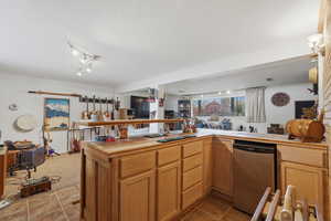 Kitchen with open floor plan, stainless steel dishwasher, track lighting, light tile patterned flooring, and tile counters