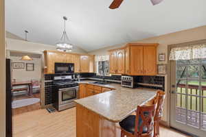 Kitchen featuring black appliances, lofted ceiling, light wood-type flooring, backsplash, and a breakfast bar area