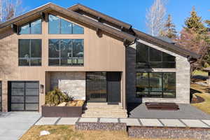 Contemporary house featuring stone siding, a garage, concrete driveway, and entry steps