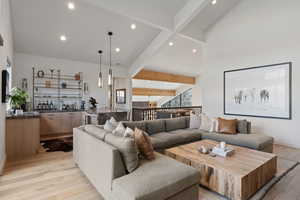 Living room with light wood-style flooring, bar with sink, lofted ceiling, and recessed lighting