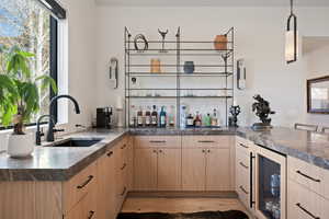Indoor wet bar with light wood finish cabinets, healthy amount of natural light, wine cooler, and hanging light fixtures