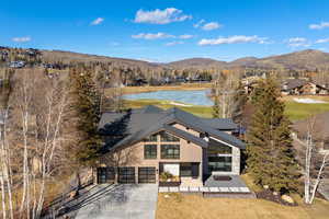 View of front of home with concrete driveway, a water and mountain view, stone siding, a front yard, and view of golf course