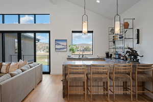 Indoor wet bar with light wood-style floors, vaulted ceiling, and pendant lighting
