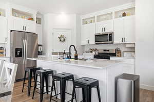 Kitchen with open shelves, stainless steel appliances, white cabinets, and a kitchen island with sink