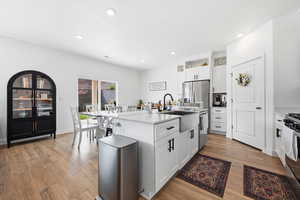 Kitchen featuring a kitchen island with sink, white cabinetry, stainless steel appliances, light wood-type flooring, and recessed lighting