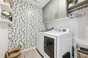 Laundry room with wallpapered walls, light wood-type flooring, cabinet space, and separate washer and dryer