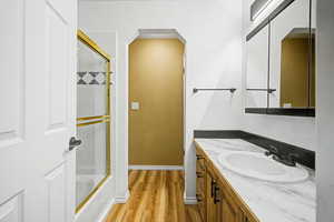 Full bath featuring vanity, enclosed tub / shower combo, and light wood-style floors