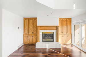 Unfurnished living room with dark wood-style floors and a tiled fireplace