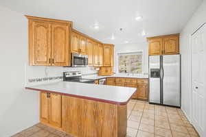 Kitchen with stainless steel appliances, light tile patterned floors, a peninsula, wood finish cabinets, and recessed lighting
