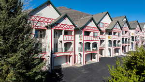 View of front of home with a garage, driveway, a balcony, stucco siding, and roof with shingles