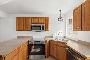 Kitchen with stainless steel appliances, a peninsula, wood finish cabinets, hanging light fixtures, and light countertops
