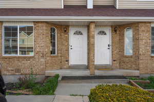 Entrance to property with covered porch, brick siding, and roof with shingles