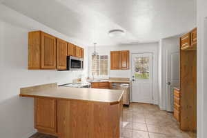 Kitchen with wood finish cabinets, light countertops, a peninsula, stainless steel appliances, and a textured ceiling