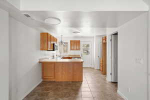 Kitchen with light countertops, wood finish cabinets, a peninsula, hanging light fixtures, and a textured ceiling