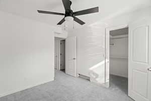Unfurnished bedroom featuring a walk in closet, light carpet, and ceiling fan