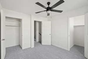 Unfurnished bedroom featuring light colored carpet, ceiling fan, and a walk in closet