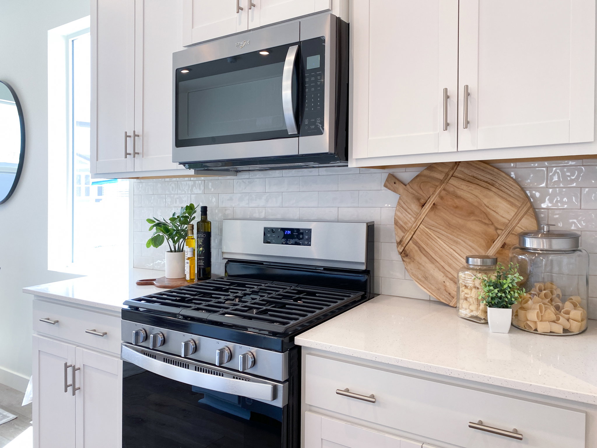 Example: Kitchen with stainless steel appliances, light stone counters, white cabinets, decorative backsplash, and plenty of natural light