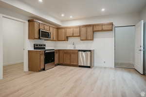 Example of basement Kitchen featuring stainless steel appliances, wood finish cabinets, light countertops, light wood-type flooring, and recessed lighting
