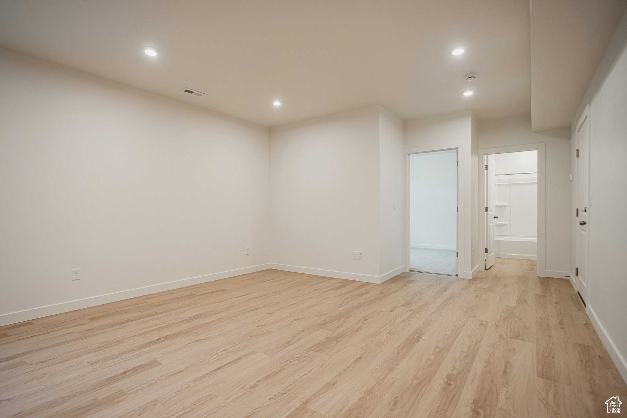 Example of basement - Unfurnished room with light wood-style floors and recessed lighting