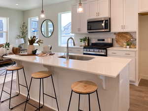 Example: Kitchen with white cabinets, stainless steel appliances, hanging light fixtures, and light stone counters