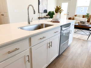 Example: Kitchen featuring light wood-type flooring, light stone countertops, white cabinetry, stainless steel dishwasher, and open floor plan
