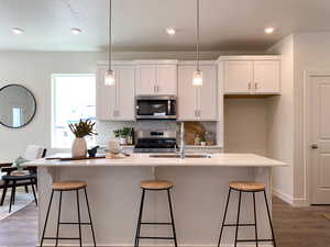 Example: Kitchen featuring a breakfast bar, dark wood-style flooring, a center island with sink, and white cabinets