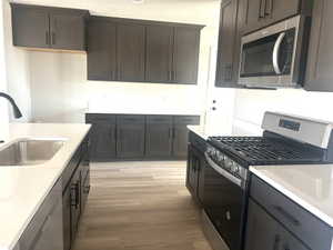 Modern kitchen featuring dark wood-finish cabinetry, light countertops, wood-finish flooring, a stainless steel range, and a stainless steel microwave