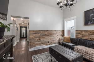 Living room with dark wood-type flooring, wainscoting, wood walls, and suspended lighting