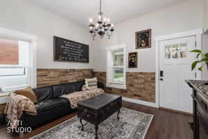 Living area with a wainscoted wall, healthy amount of natural light, dark wood-type flooring, hanging lights, and wooden walls