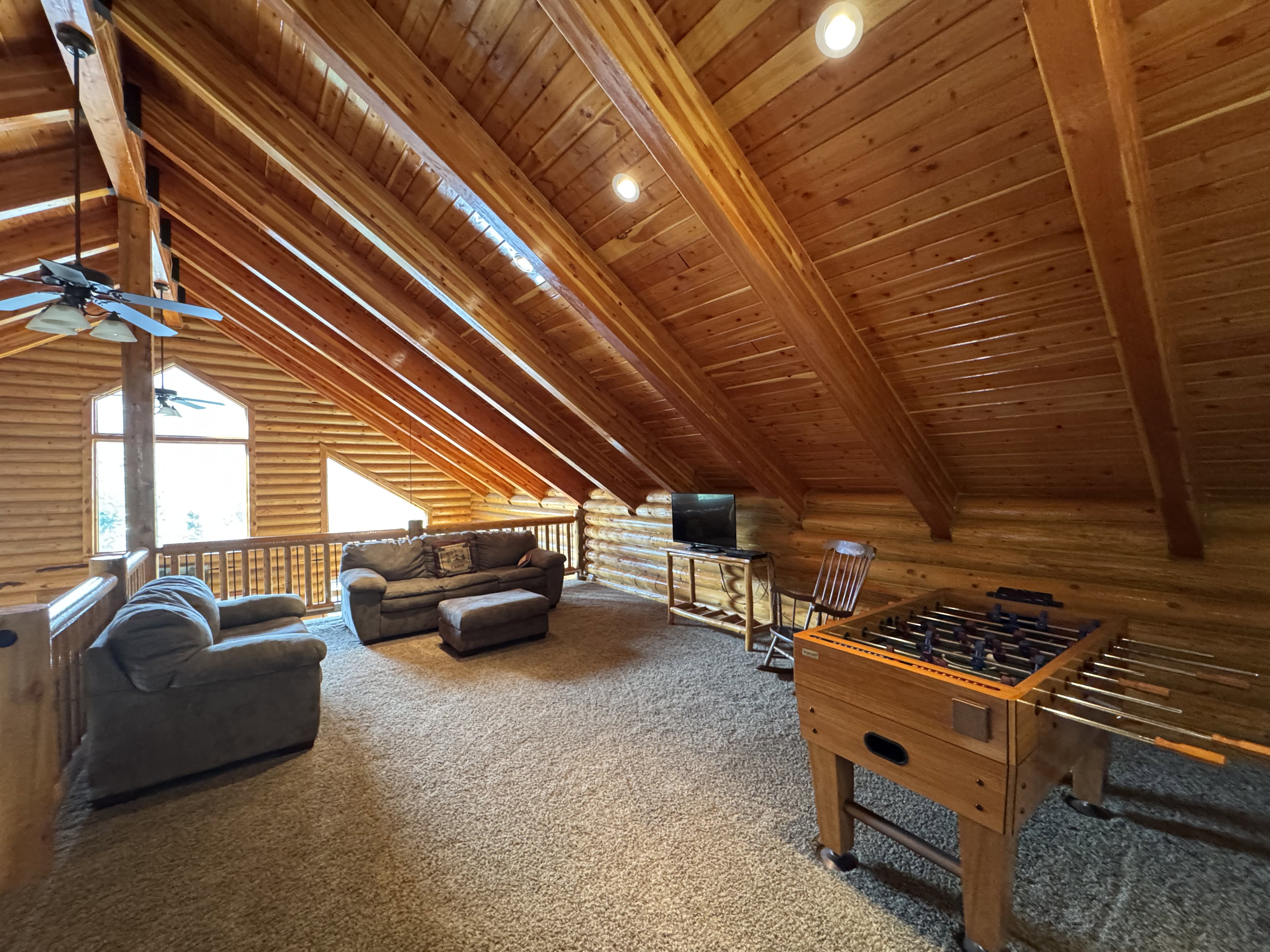 Loft  featuring log walls, carpet floors, a ceiling fan, and a wooden ceiling with exposed beams