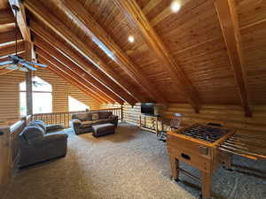 Loft  featuring log walls, carpet floors, a ceiling fan, and a wooden ceiling with exposed beams